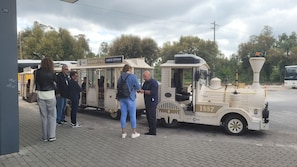 A vintage train with passengers boarding, parked on a paved area with trees in the background.