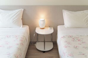 Una habitación de hotel con dos camas individuales, una mesita de noche con lámpara y un enchufe.