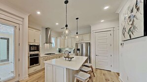 Una cocina moderna con armarios blancos, una isla central, electrodomésticos de acero inoxidable e iluminación colgante.