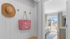 Una habitación de hotel con un banco de madera, un sombrero de paja y un bolso a rayas en la pared.