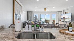 Una cocina moderna con una isla grande, pileta de acero inoxidable y un comedor con vista al océano.