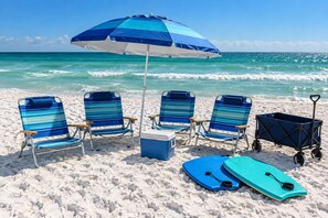 A beach scene with four striped beach chairs, a cooler, a blue paddleboard, and a beach cart.