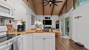 A modern kitchen with white cabinets, a wooden countertop, and a ceiling fan.