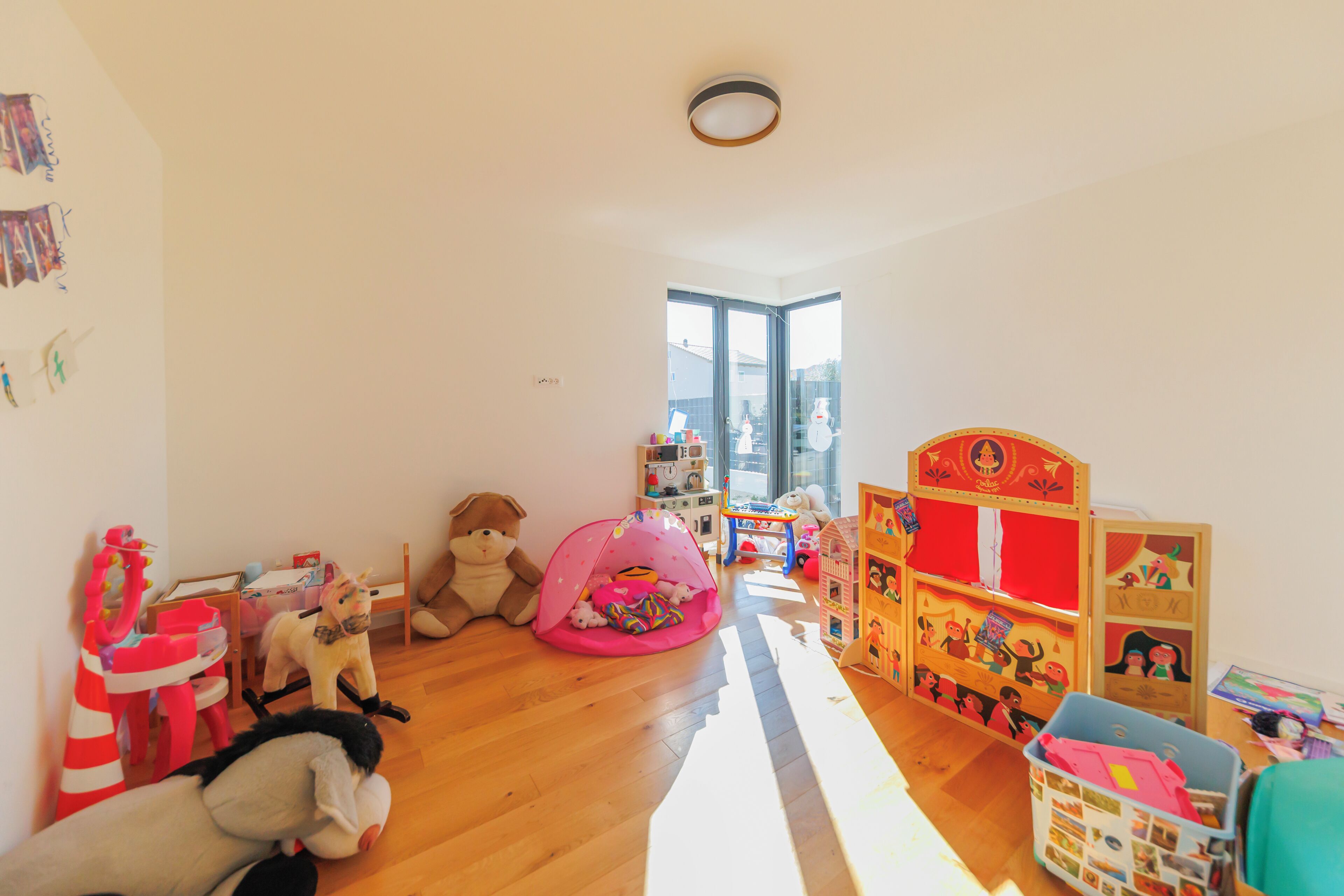 A child's playroom with toys, a pink play tent, and a wooden bookshelf.