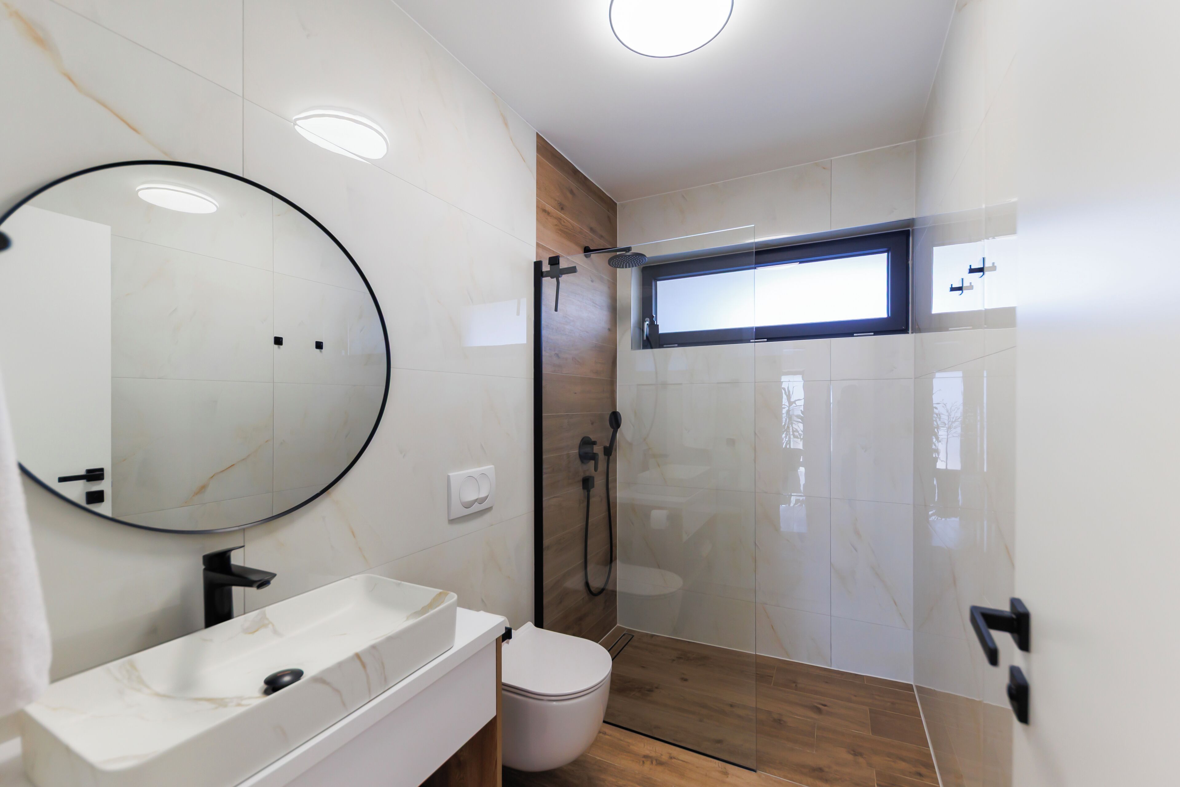 A modern bathroom with a marble sink, a toilet, and a glass-enclosed shower area.