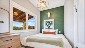 A bedroom with a bed, a dresser, a window with a view, a wall-mounted light fixture, and a decorative skull.