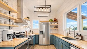 A modern kitchen with a stainless steel refrigerator, wooden countertops, and teal cabinetry.