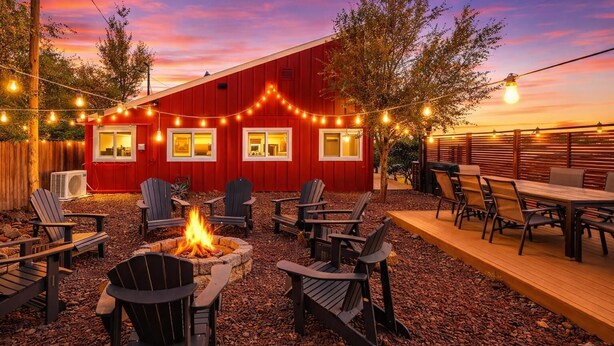 A red building with string lights, outdoor seating, and a fire pit.