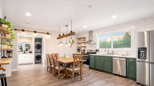 Una cocina moderna con suelo de madera, comedor con mesa y sillas de madera, electrodomésticos de acero inoxidable y vistas a zonas verdes.