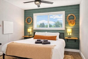 A bedroom with a bed, two bedside lamps, a window with blinds, and a ceiling fan.