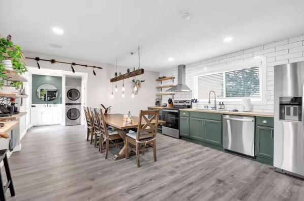 Cocina moderna con mesa y sillas de madera, armarios verdes y horno empotrado.