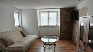 Ein Zimmer mit einer Couch, einem Glastisch, einer Heizung, einer Steinwand und einem Schrank mit einem Fernseher.