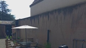 Eine Terrasse im Freien mit Tisch und Stühlen, einem Grill und Kübelpflanzen.