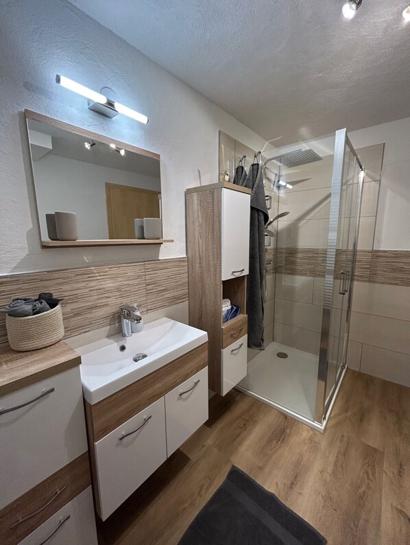 A modern bathroom with a wooden vanity, a glass shower enclosure, and a large mirror.