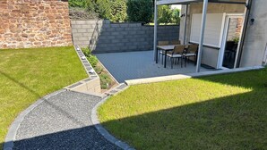 Een terras met een stenen muur, een grindpad en een gazon.