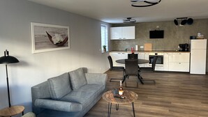 Een moderne woonkamer met een grijze bank, een ronde salontafel en een eethoek met een kleine tafel en stoelen.