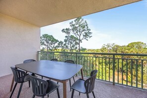 A balcony with a table and chairs, a view of trees, and a green railing. - Luxury Condo with Sanctuary Views Merritt Island (Merritt Island)