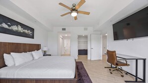 Ein Hotelzimmer mit einem Bett, einem Schreibtisch, einem Sessel, einem Deckenventilator, einem Fernseher und einem Gemälde an der Wand.