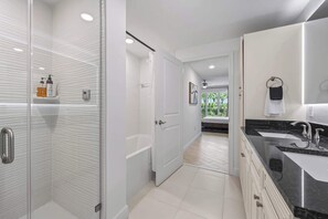 A modern bathroom with a glass shower enclosure, a bathtub, a vanity with a double sink, and a door leading to a balcony with a view. - Luxury Condo with Sanctuary Views Merritt Island (Merritt Island)