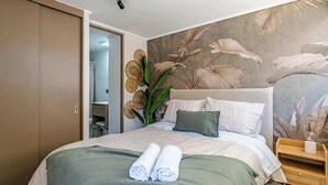 A neatly made bed with rolled towels, a headboard with a floral mural, and a wooden nightstand with a decorative item. - Charming 1BR in Santiago, WiFi & Equipped Kitchen (Unknown)
