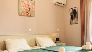 A hotel room with two beds, a green bedspread, white pillows, a painting of flowers, an air conditioner, and a wall-mounted artwork. - Spacious first floor apartment, Family-Friendly Stay Near the Beach (Corfu)