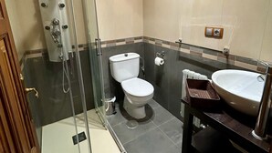 Casa de banho com cabine de chuveiro em vidro, sanita e lavatório com espelho.