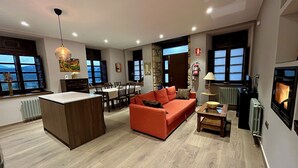 Uma sala de estar moderna com piso de madeira, um sofá vermelho, uma área de jantar com mesa e cadeiras, e uma lareira.