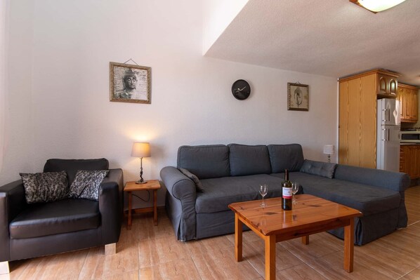 A living room with a black leather sofa, a grey sectional sofa, a wooden coffee table, and a wall clock.