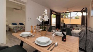 Un coin repas avec une table dressée pour deux personnes, une bouteille de vin et un vase rempli de fleurs blanches.