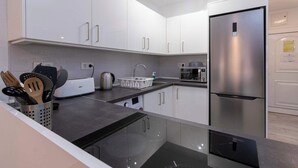 Une cuisine moderne avec des meubles blancs, un réfrigérateur en acier inoxydable et un four encastré.