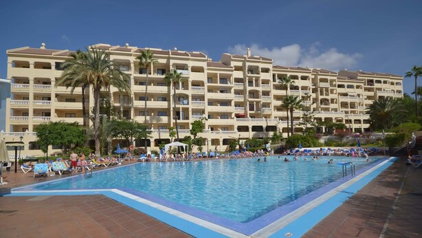 Un espace piscine d’hôtel doté de plusieurs niveaux de balcons, de palmiers et de chaises longues.