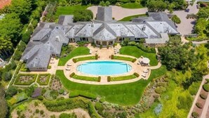 Vista aérea de una extensa propiedad con una piscina central, rodeada de jardines cuidados y una distribución simétrica.
