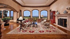 Un salón amplio con un tapiz grande y elaborado, varias zonas de estar y una chimenea.