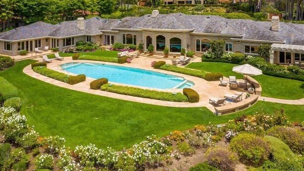 Una amplia casa de dos pisos con piscina, rodeada de césped y jardines bien cuidados.