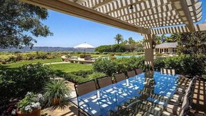 Una mesa de comedor con cubierta de vidrio, sillas, una pérgola, una piscina y vistas del paisaje.