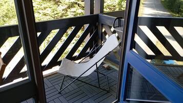 A balcony with a white hammock chair, wooden floor, and a view of a road and greenery.