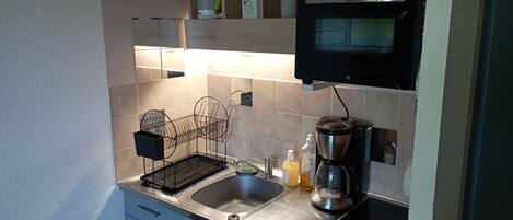 Una cocina compacta con un lavamanos, una cafetera y un microondas.