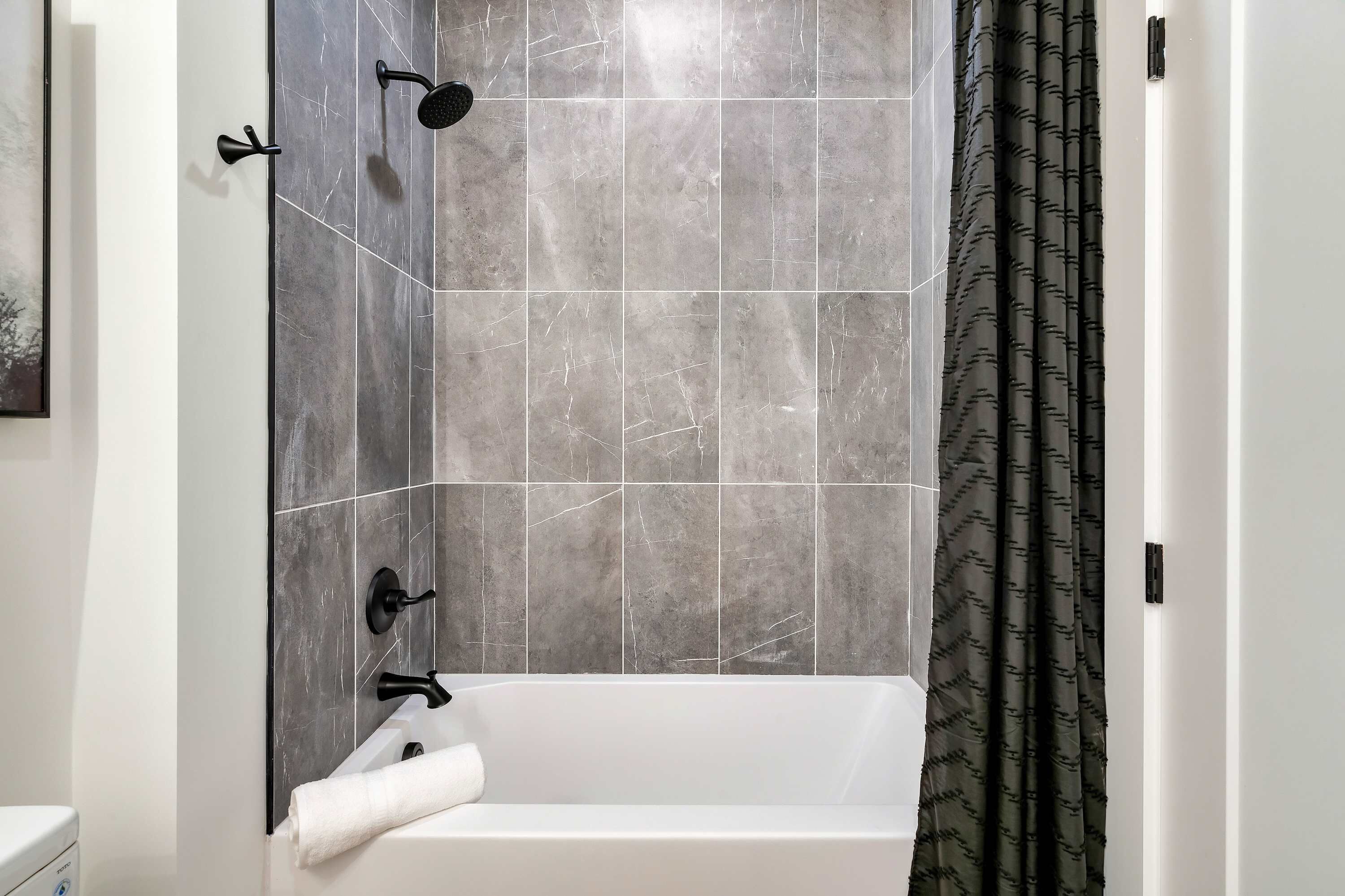Un baño con una bañera blanca, una toalla y una ducha con accesorios negros.