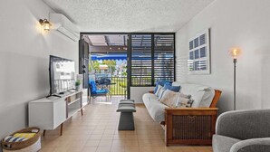 Una sala de estar moderna con un sofá, una mesita, una cesta y un televisor sobre un mueble blanco.