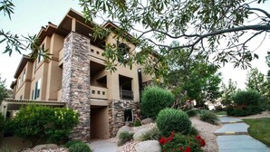 A multi-story residential building with a stone facade, a balcony, and a landscaped garden with red flowers and shrubs. - Redterra - A Stunning Escape! (Hurricane)
