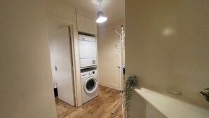 A laundry area with a washing machine and dryer, a small stool, and a plant. - 2 Bed Apartment/ Tower Bridge / Big Ben /the Shard (London)