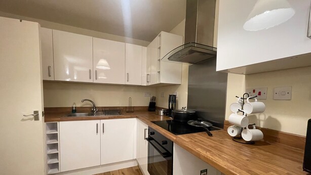 A modern kitchen with white cabinets, a stainless steel range hood, a black induction cooktop, and a coffee maker. - 2 Bed Apartment/ Tower Bridge / Big Ben /the Shard (London)
