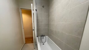A narrow bathroom with a bathtub, tiled walls, and a wooden floor. - 2 Bed Apartment/ Tower Bridge / Big Ben /the Shard (London)