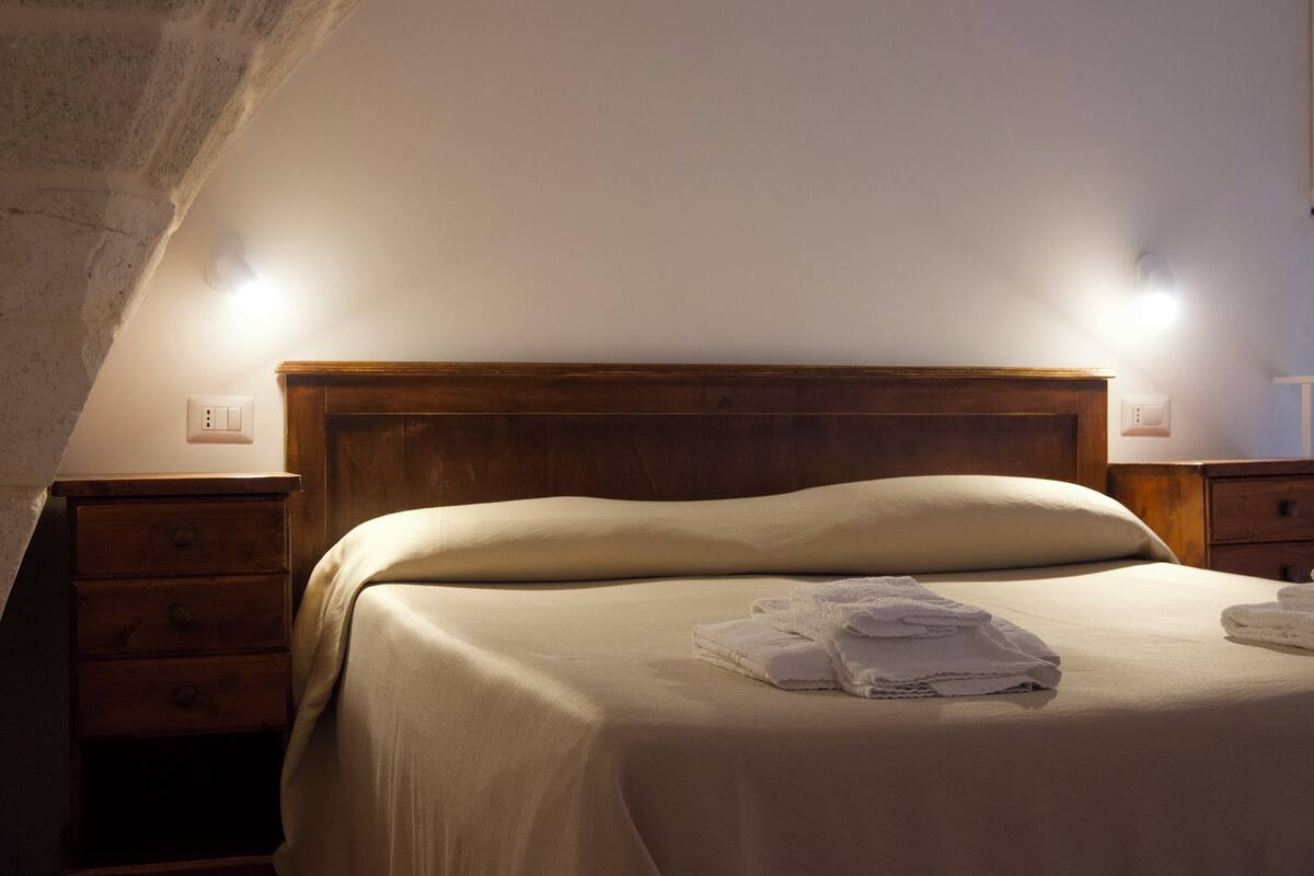 Ein ordentlich bezogenes Bett mit Holzkopfbrett, zwei Nachttischen und einer Wandleuchte.