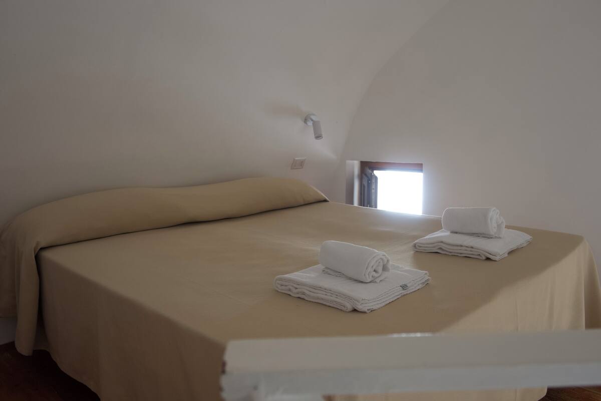 Ein Schlafzimmer mit einem Bett, beiger Bettwäsche und zwei gefalteten Handtüchern auf dem Bett.