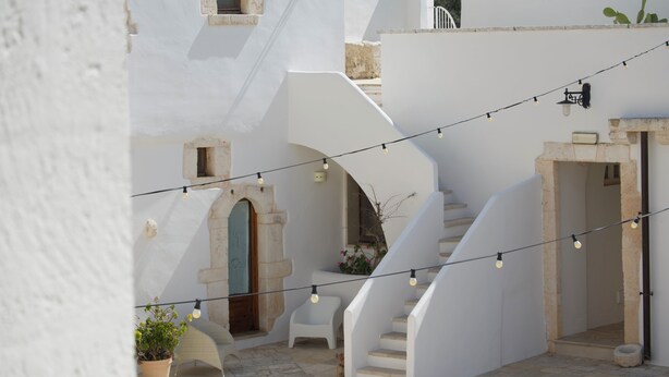 A courtyard with white walls, a stone staircase, and string lights. - masseria casamassima (Ostuni)