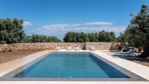 A rectangular swimming pool with a stone wall and a few lounge chairs. - masseria casamassima (Ostuni)