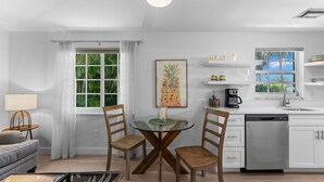 A modern kitchen with white cabinets, a dishwasher, and a window with a view of greenery. - 541 SeaScape Cottage · Walk2Beach (Naples)