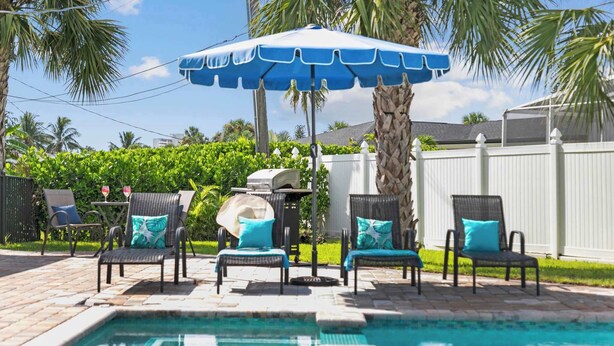 A pool area with lounge chairs, a grill, and a white fence. - 541 SeaScape Cottage · Walk2Beach (Naples)