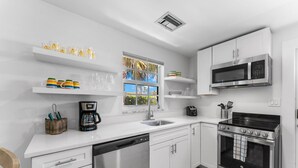 A modern kitchen with white cabinets, a stainless steel dishwasher, a built-in oven, and a microwave. - 541 SeaScape Cottage · Walk2Beach (Naples)